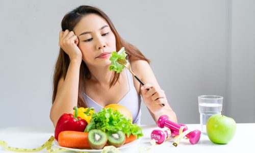 Symptoms of anorexia manifested in aversion to food. Portrait of young Asian woman in unsatisfied facial emotional expression, refusing to eat vetables and fruits. Close up